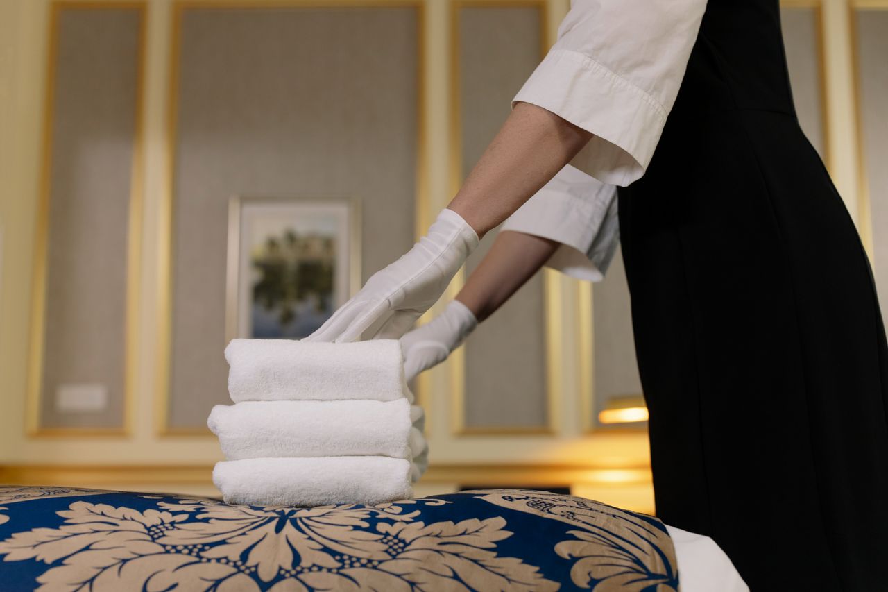 Une femme de chambre d’hôtel empile soigneusement des serviettes fraîches dans un décor de chambre luxueuse.